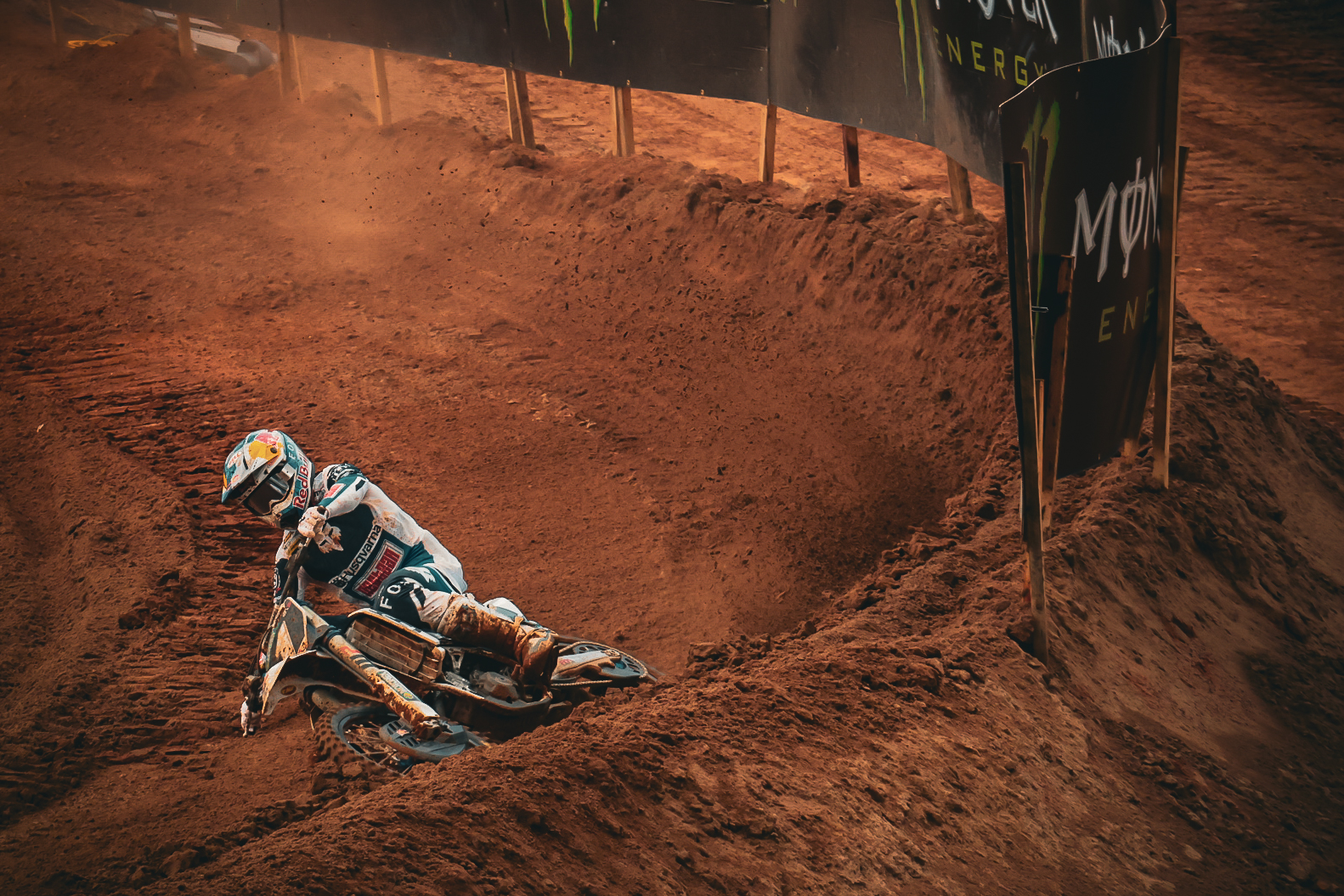 Motocross rider carving through a red dirt berm